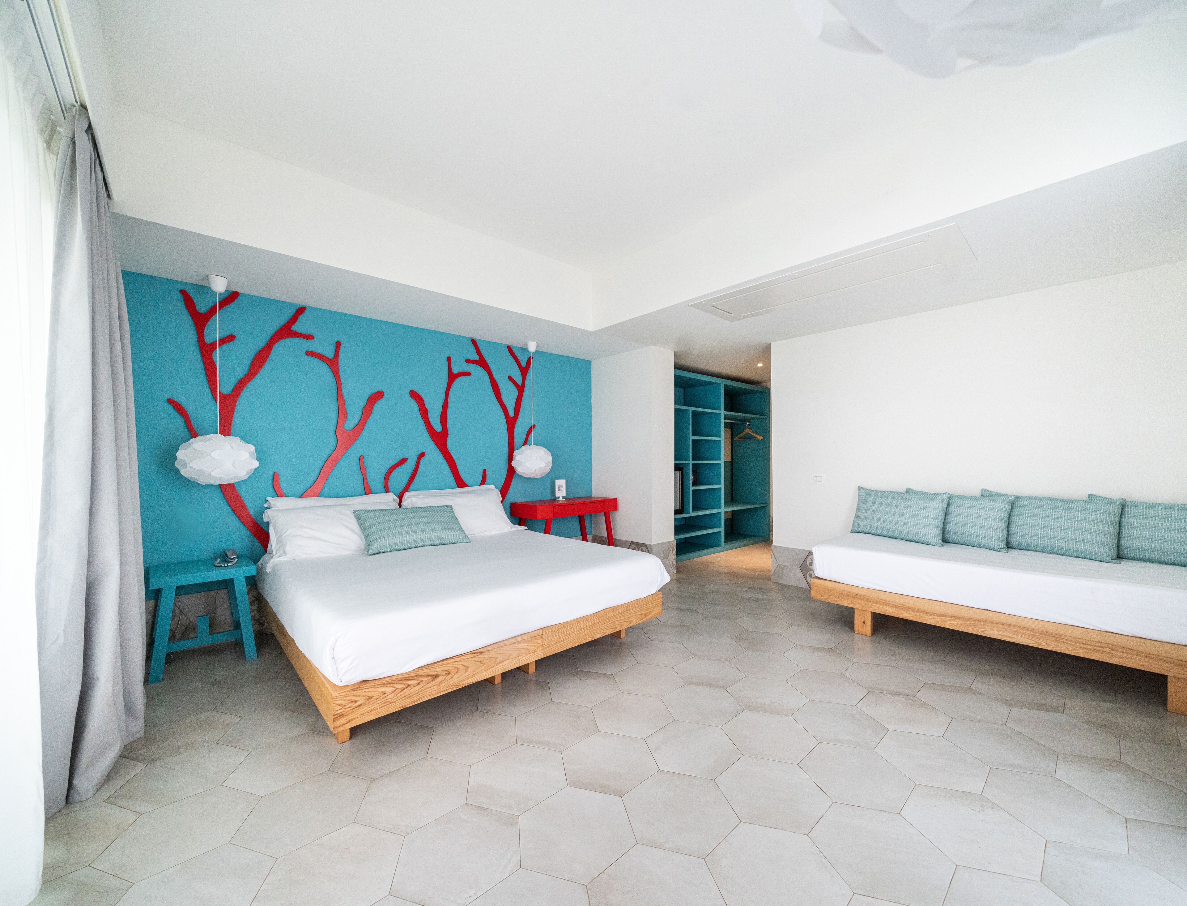 A modern bedroom with two beds, a blue accent wall, and a closet with hanging space.