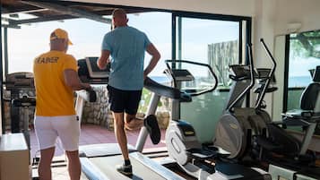 A gym with treadmills and exercise equipment, a stone wall, and a view of the ocean.
