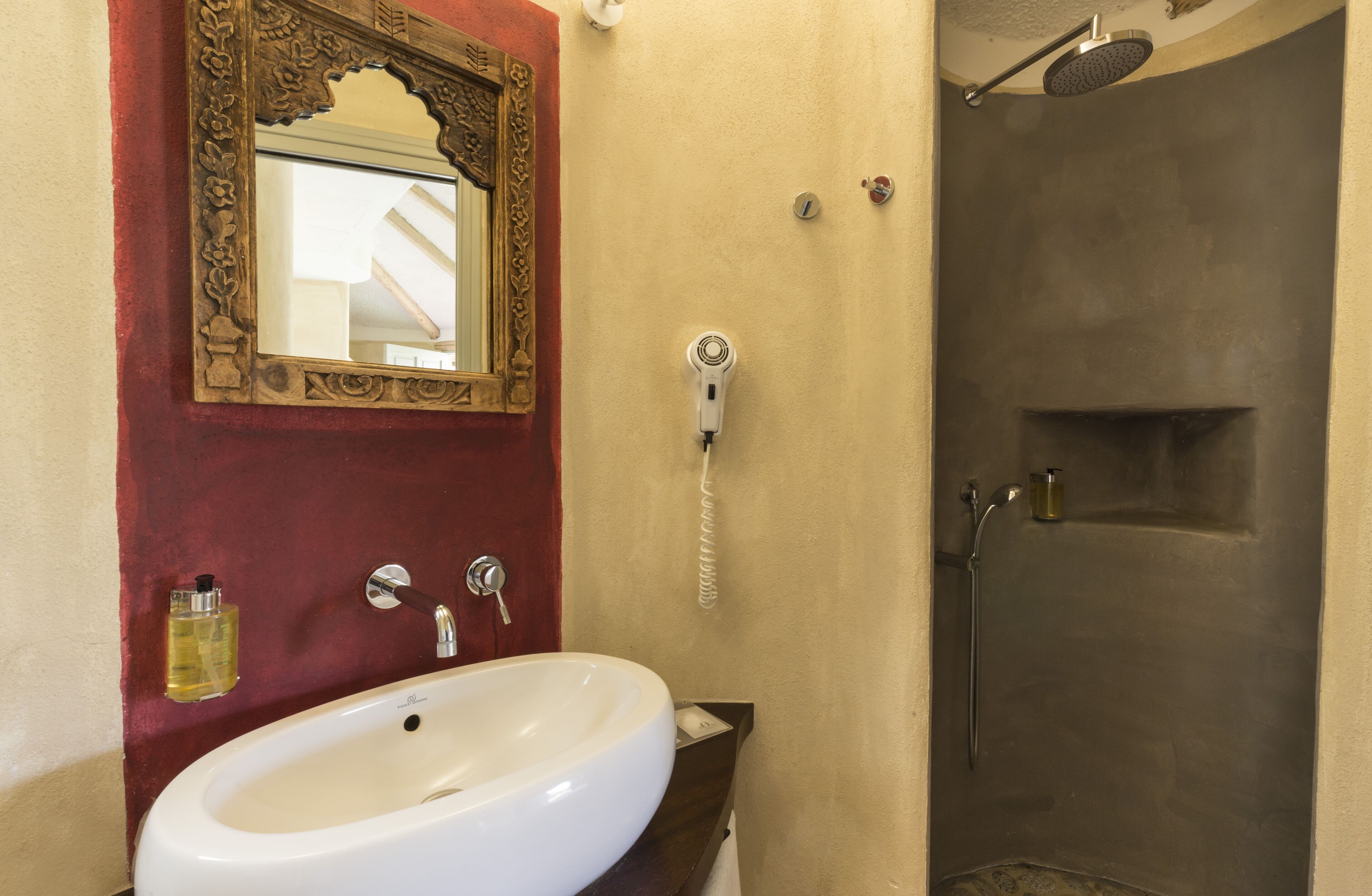 A bathroom with a white sink, a mirror with an ornate frame, a hairdryer, and a shower.