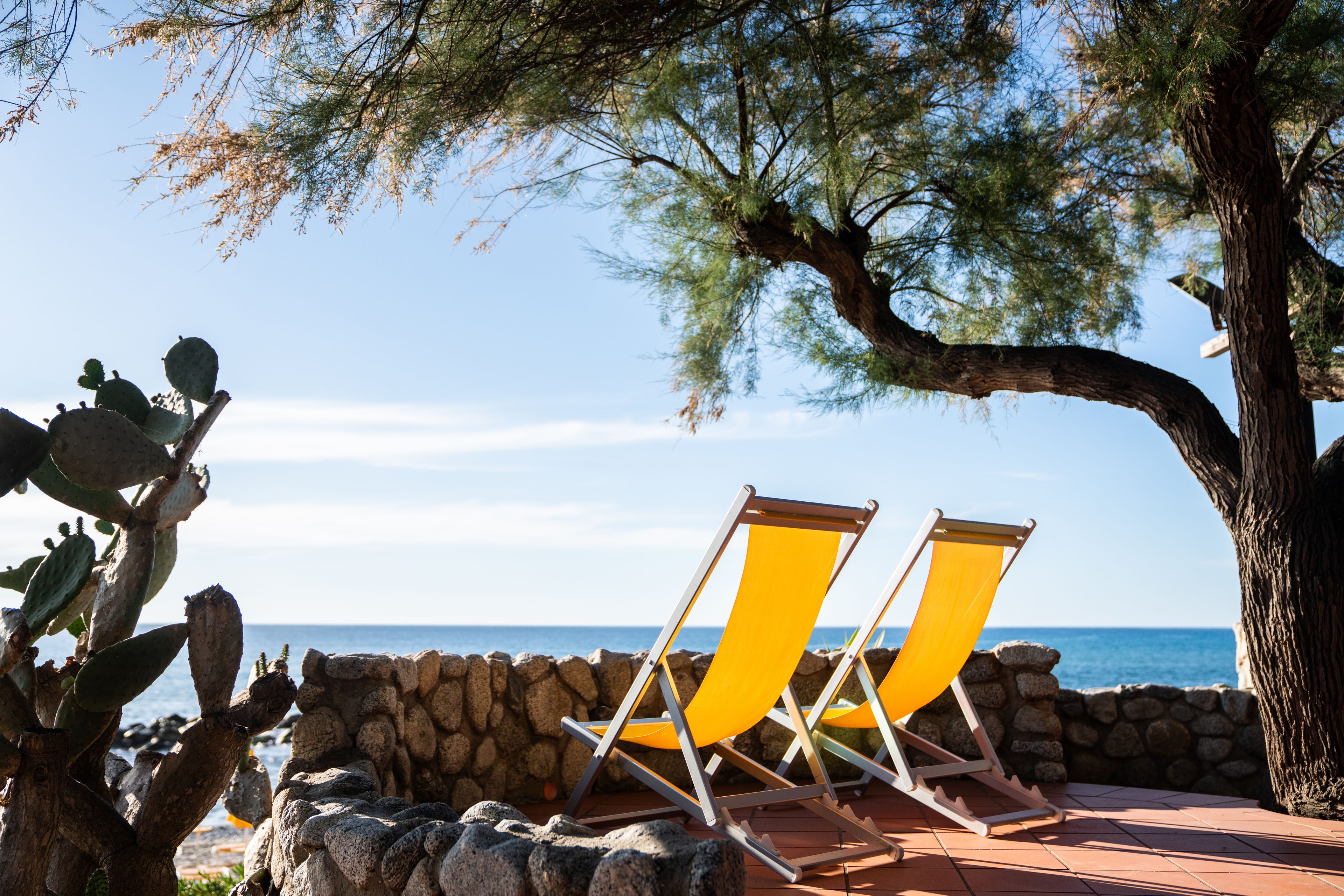 Two yellow beach chairs by a stone wall overlooking the sea.