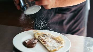 A person sprinkling powdered sugar on a crepe with chocolate sauce on a plate.