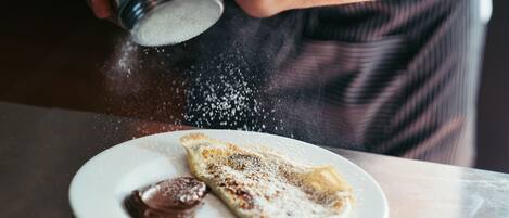 A person sprinkling powdered sugar on a crepe with chocolate sauce on a plate.