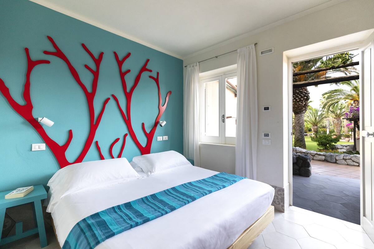 A bedroom with a bed, a nightstand, and a view of the outdoor area.