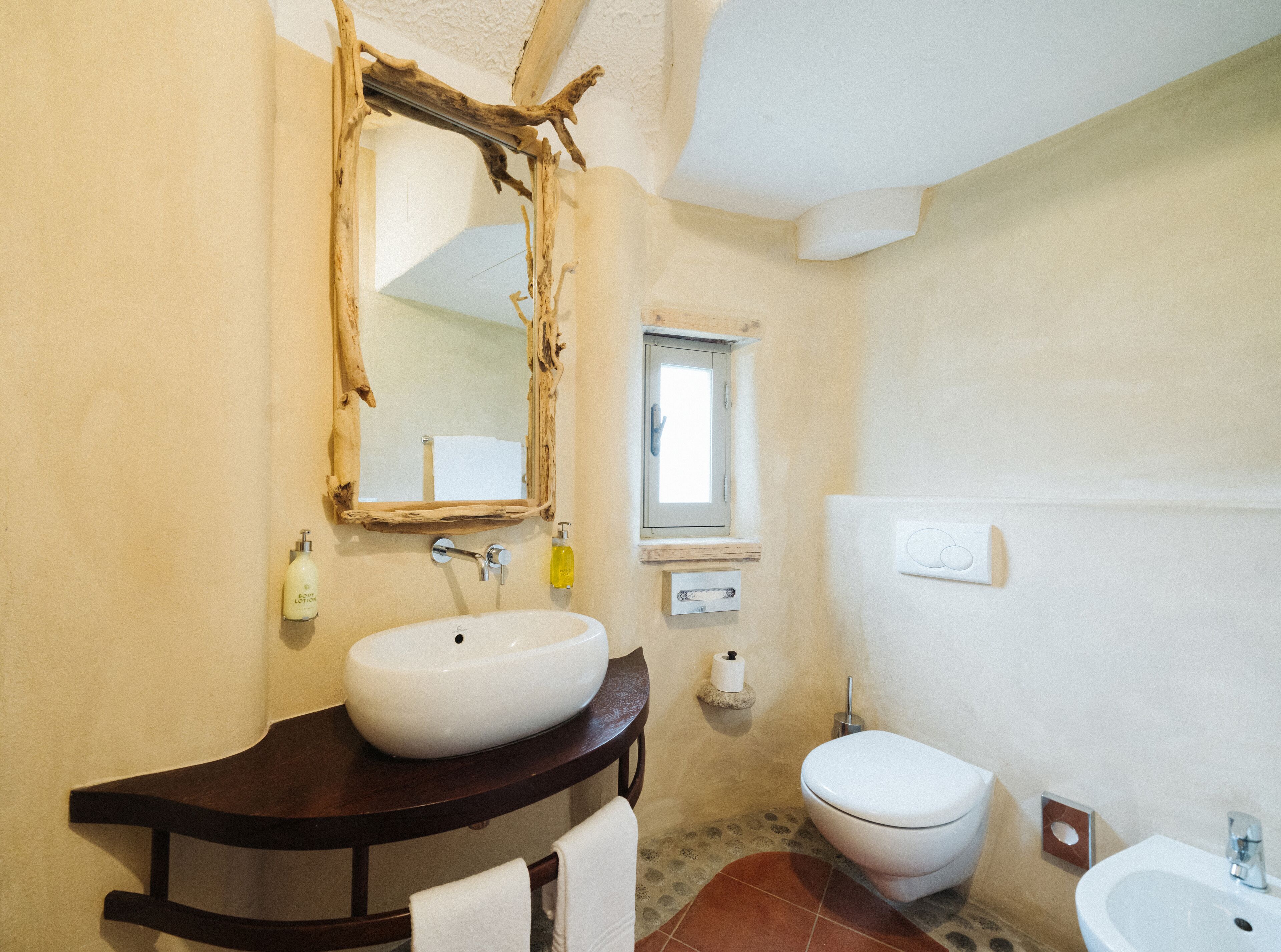 A bathroom with a wooden vanity, a white sink, a toilet, and a mirror with a rustic frame.