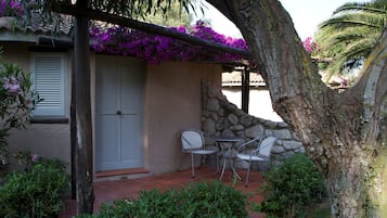 Un patio con dos sillas de metal y una pequeña mesa, un muro de piedra y una puerta con contraventanas.