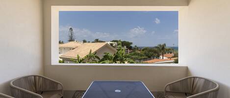 A balcony with a table and two chairs, overlooking a residential area with houses and greenery.