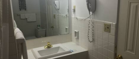 Ett badrum med ett vitt handfat, en spegel, en hårtork och en handduksställning.
