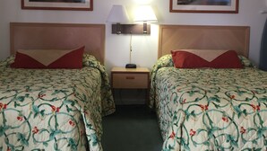 A hotel room with two beds, each with floral-patterned bedding and red pillows. There is a nightstand with a lamp between the beds. - Prestige Inn West Lafayette (West Lafayette)