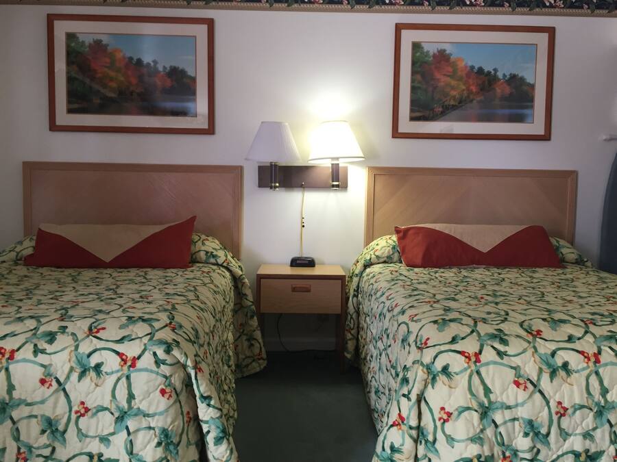 A hotel room with two beds, each with floral-patterned bedding and red pillows. There is a nightstand with a lamp between the beds.