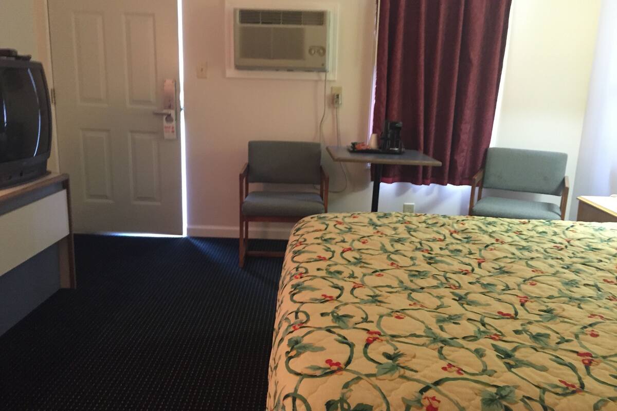 Ett hotellrum med en säng, två stolar, ett litet bord och en tv.