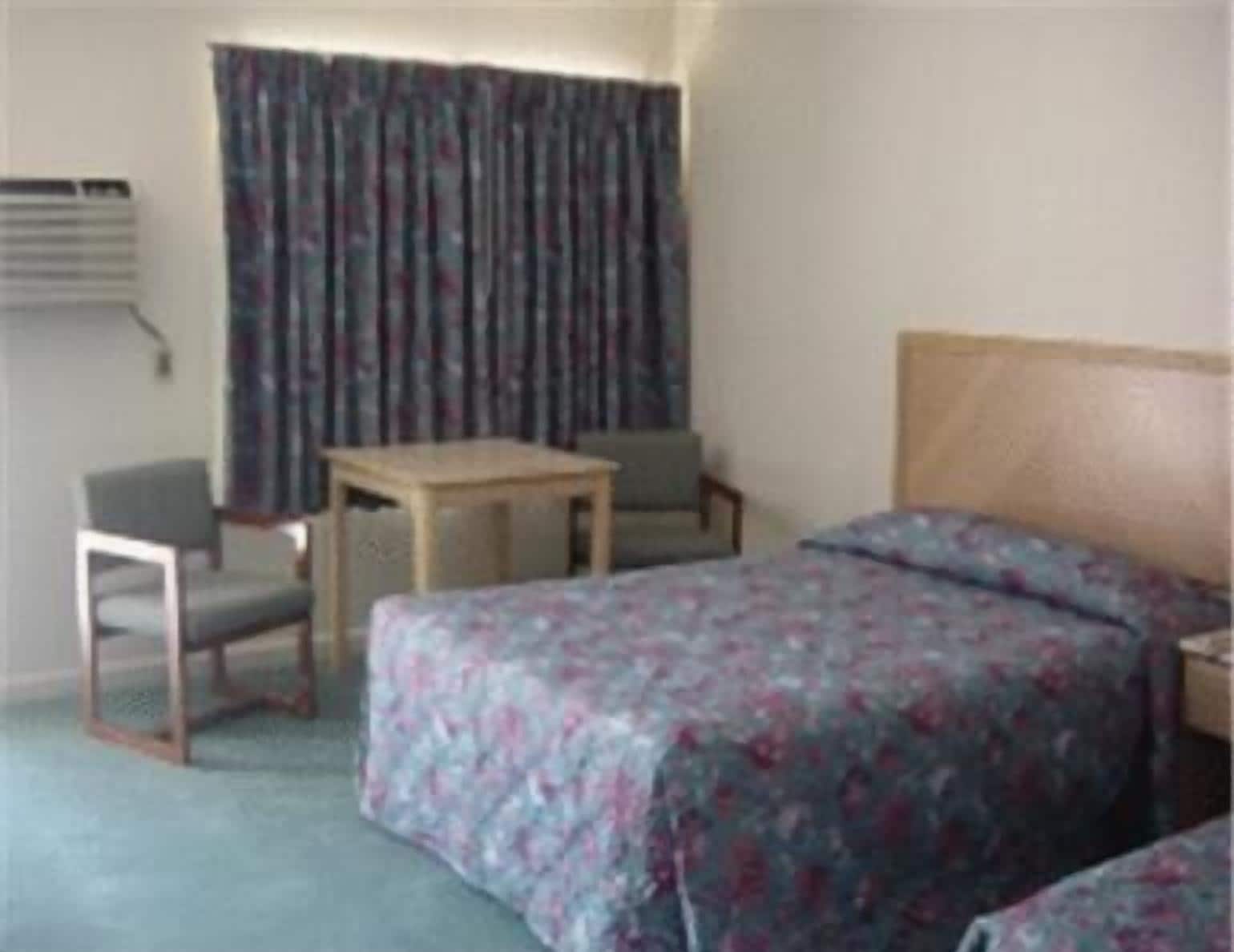 Une chambre d’hôtel avec un lit, un bureau, deux chaises et une fenêtre avec des rideaux.