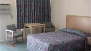 A hotel room with a bed, a desk, two chairs, and a window with curtains.