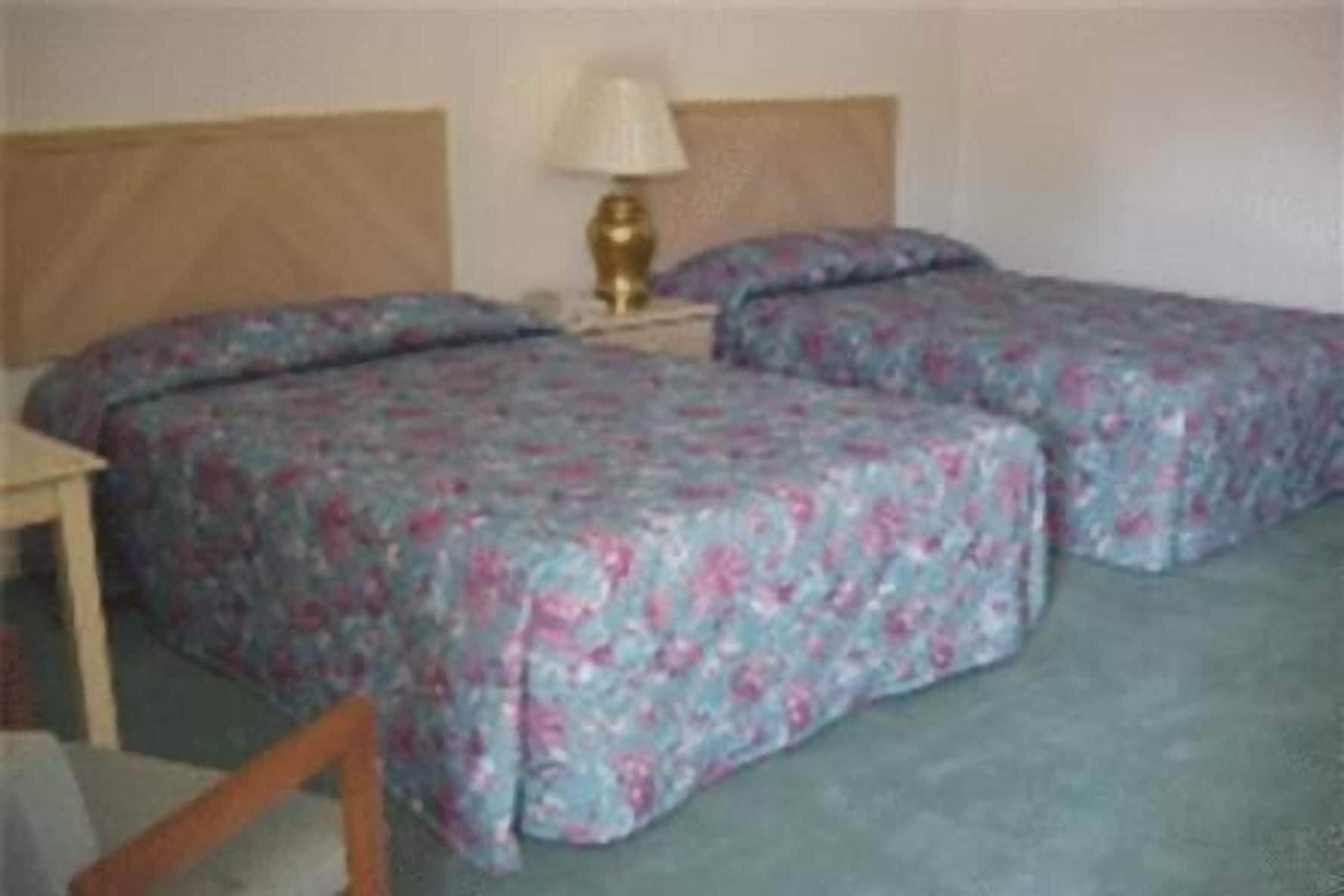 Una habitación con dos camas, una mesita de noche con lámpara y una pequeña mesa.