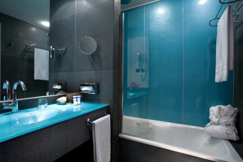 Un baño moderno con un lavabo azul, ducha con mampara de vidrio y un espejo grande.