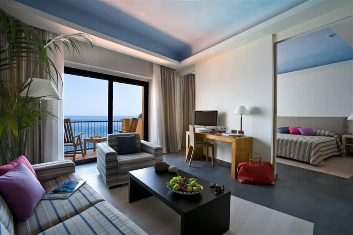 Ein modernes Hotelzimmer mit großem Balkon, einer Sitzecke, einem Essbereich und einem Bett.