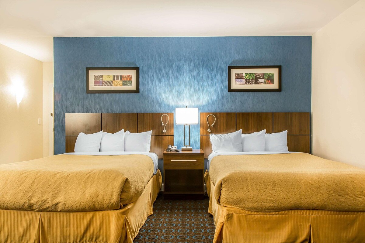 A hotel room with two beds, a nightstand with a lamp, and framed artwork on the walls.