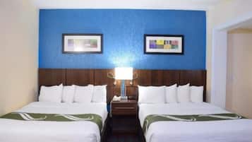 A hotel room with two beds, a wooden headboard, a nightstand, and a wall-mounted lamp.