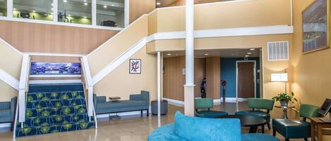 A spacious lobby with a central staircase, seating areas, and a reception desk.