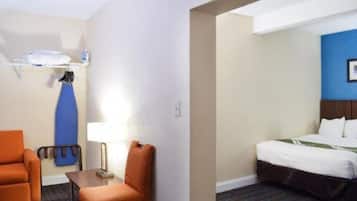 A hotel room with a bed, a chair, a small table, a lamp, and a surfboard on the wall.