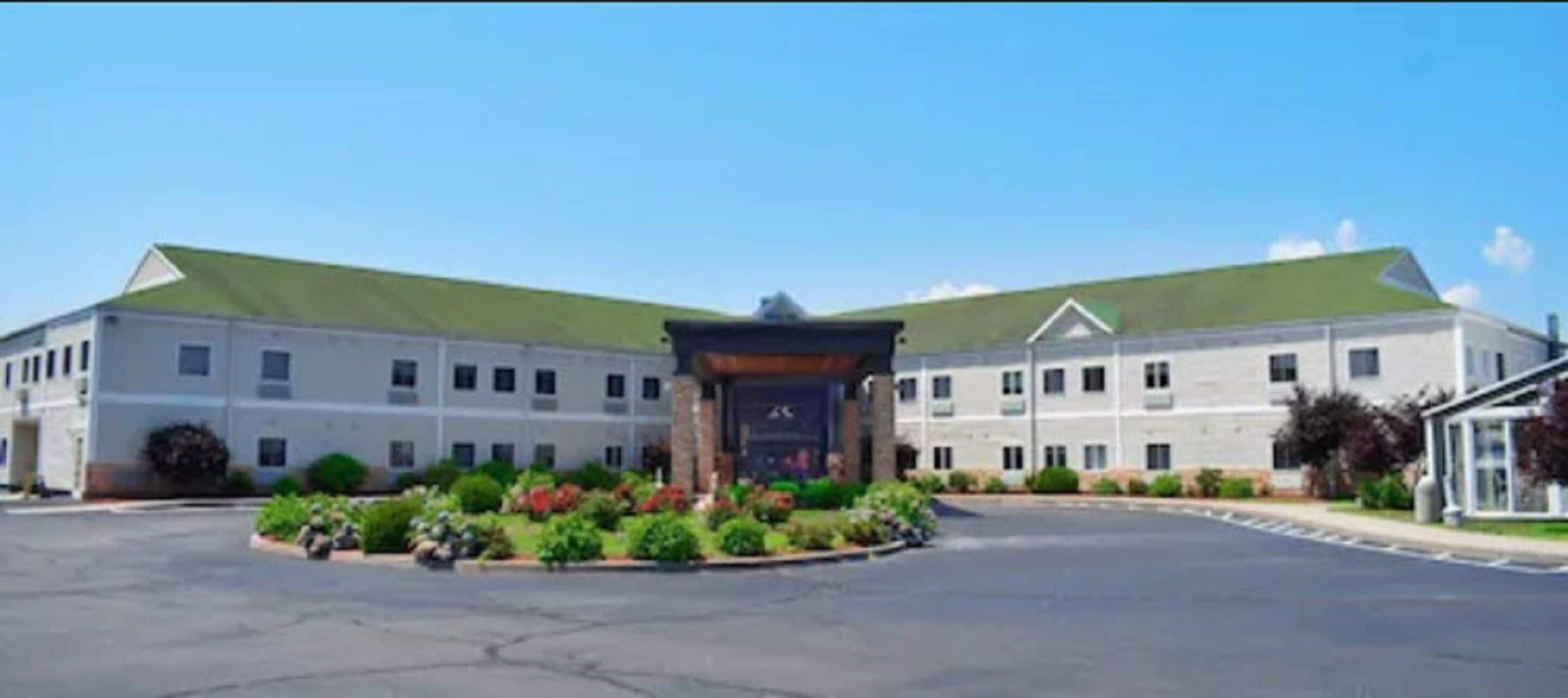 A large building with a green roof, a central entrance with a sign, and a landscaped area with plants in front.
