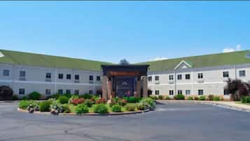 A large building with a green roof, a central entrance with a sign, and a landscaped area with plants in front.