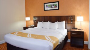 Ein Hotelzimmer mit einem großen Bett, zwei Nachttischen mit Lampen, einem hölzernen Kopfteil und einem gerahmten Bild an der Wand.