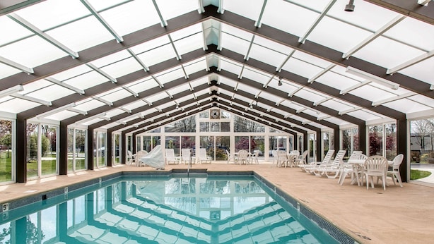 Ein überdachter Pool mit Glaswänden, Liegestühlen und Blick ins Freie.