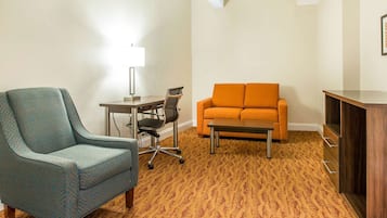 Una habitación con alfombra estampada, un sillón verde azulado, un sofá naranja, una pequeña mesa y un armario.