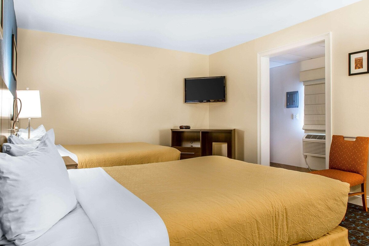 Ein Hotelzimmer mit zwei Betten, einem Fernseher, einem Schreibtisch und einem Sessel.