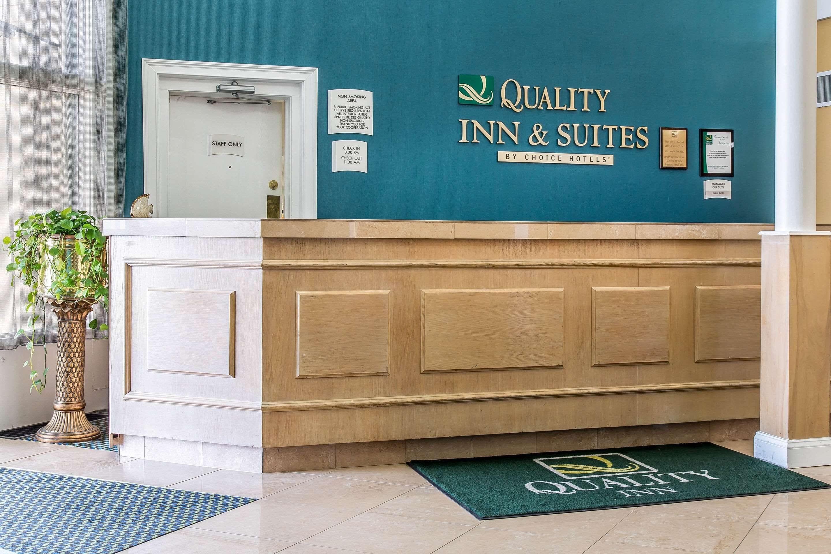 A hotel reception desk with a teal wall, a wooden counter, and a green doormat.
