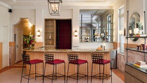 A bar area with a marble countertop, four bar stools with red cushions, and a large mirror above the counter. - Liberty Park Hotel South Beach (Miami Beach)