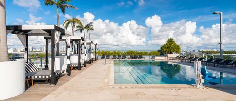 Relax by the rooftop pool surrounded by lounge chairs and palm trees overlooking the city.
