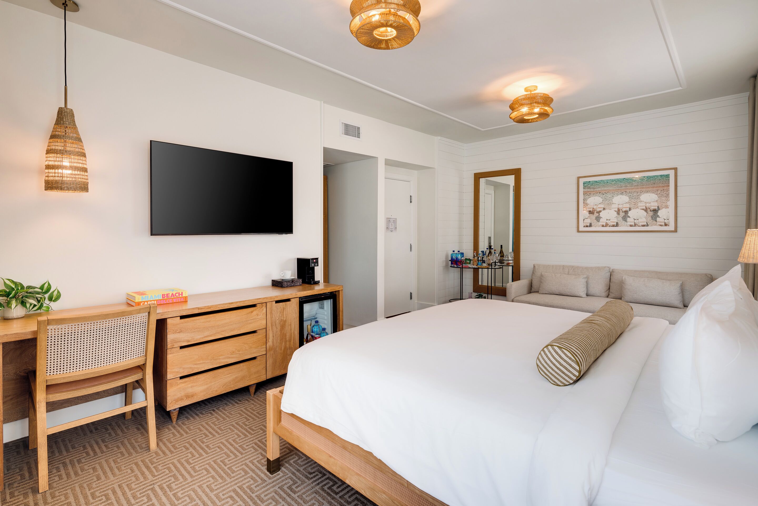A hotel room with a bed, a desk with a chair, a television, a mirror, and a painting on the wall.