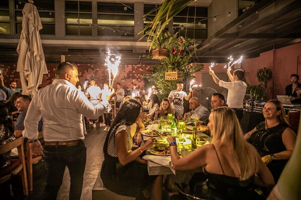 Um grupo de pessoas jantando em um restaurante, com mesas preparadas para refeições e um arranjo de planta decorativa.