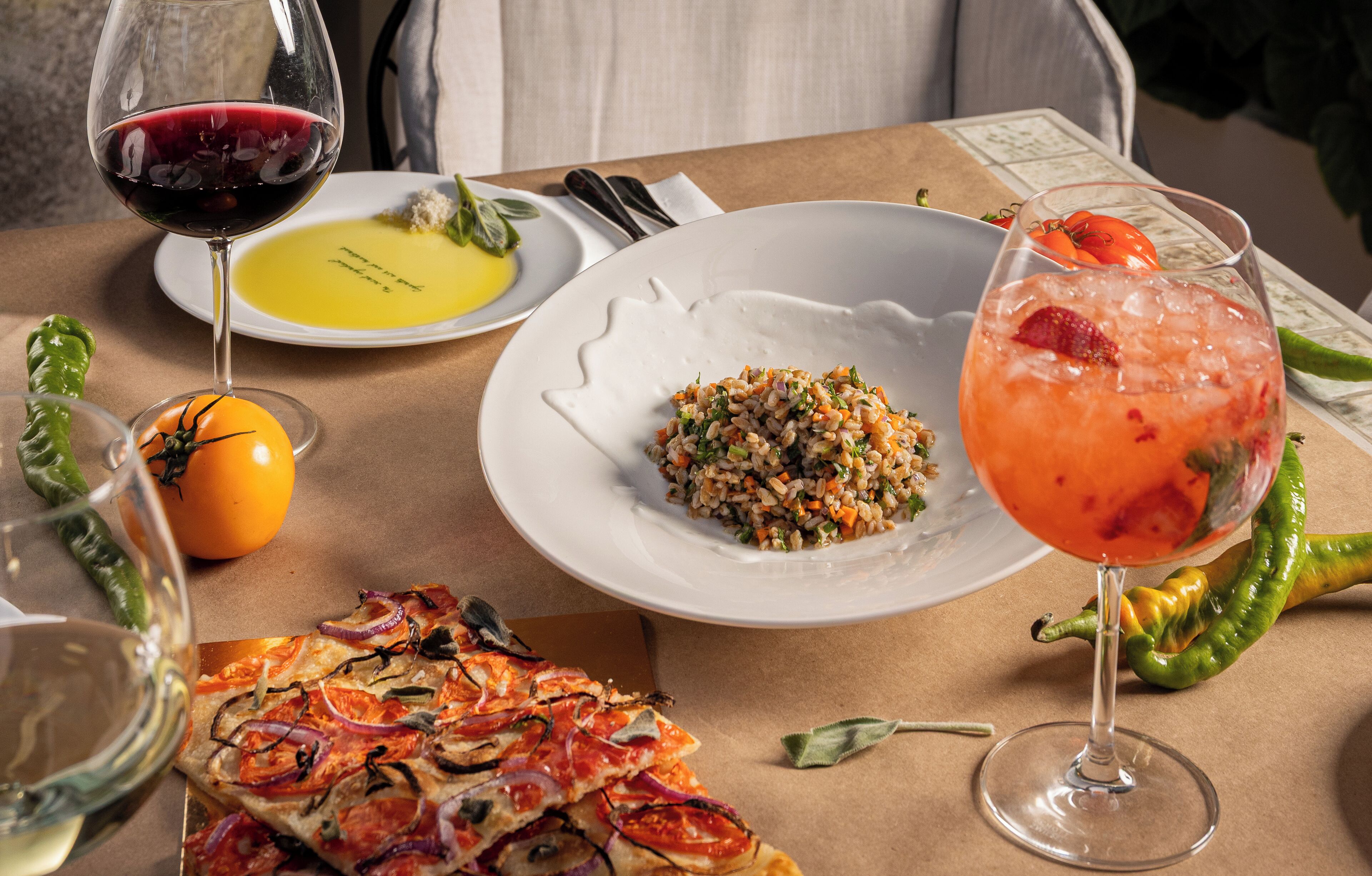A table set with a pizza, a salad, a glass of red wine, and a cocktail.
