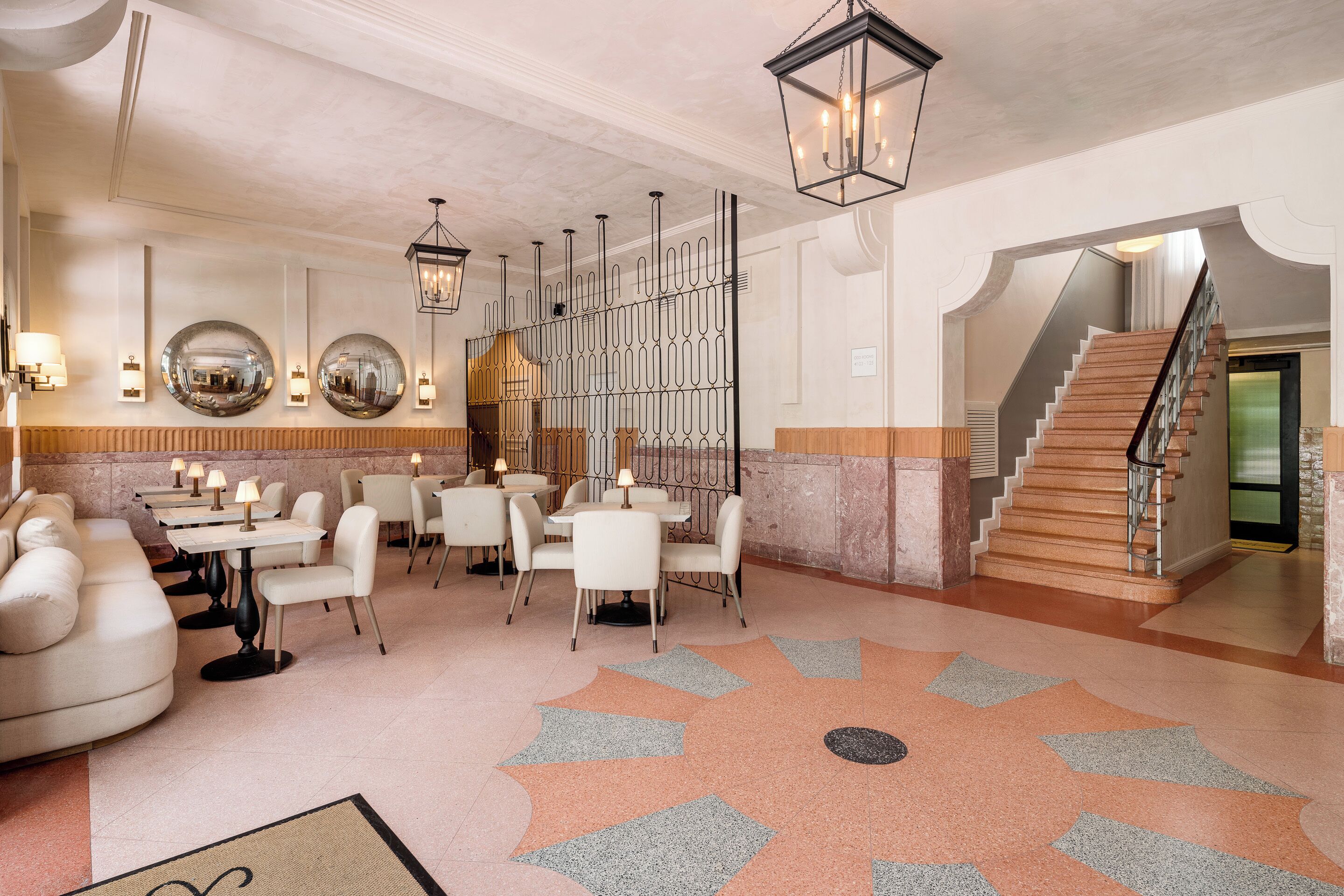 Een hotellobby met een zithoek, een trap en een decoratief vloerpatroon.