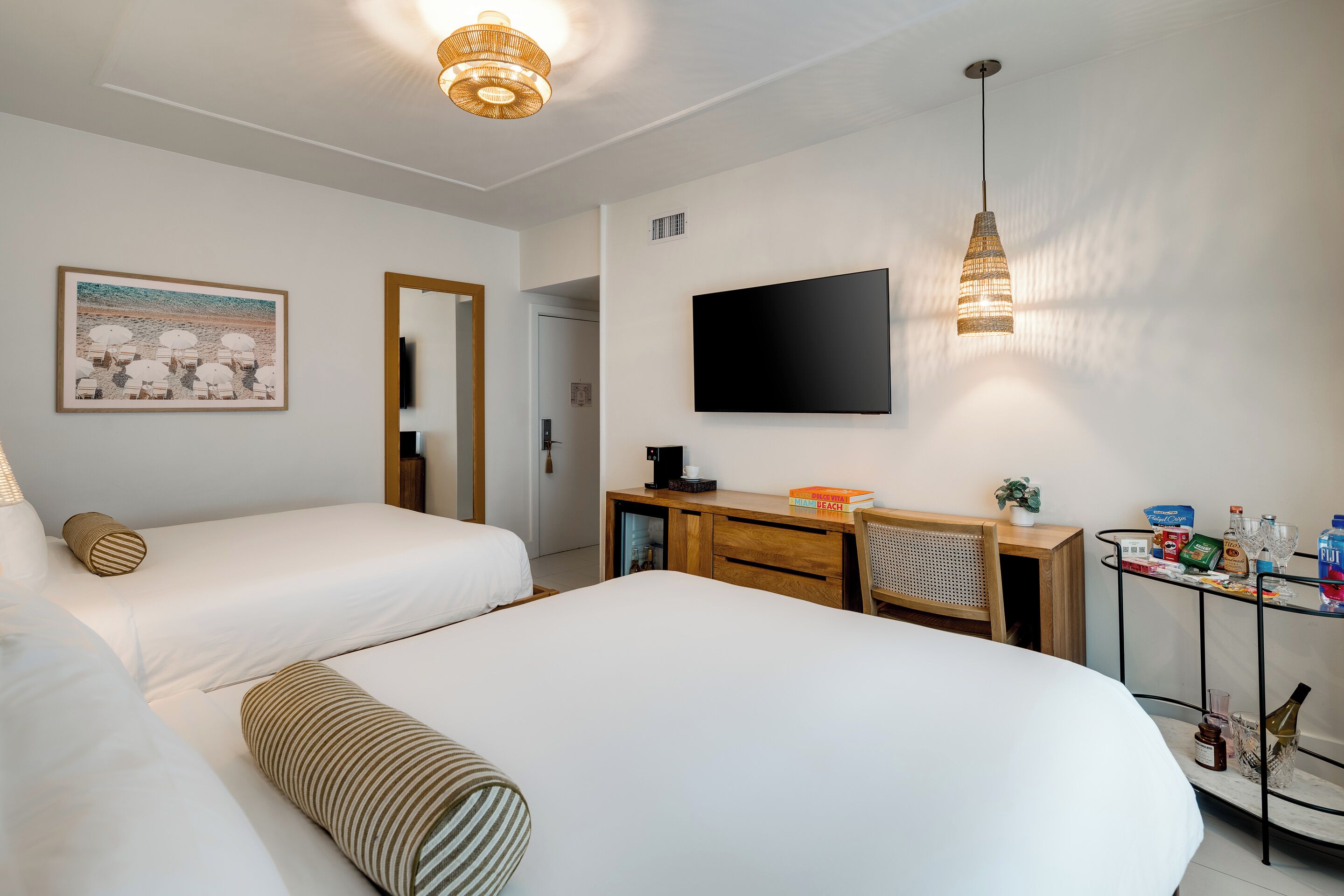 Une chambre d’hôtel avec deux lits, un bureau avec un ordinateur, un téléviseur fixé au mur et une petite table avec des boissons et des en-cas.