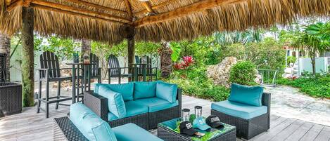 An outdoor patio with wicker furniture and a thatched roof.