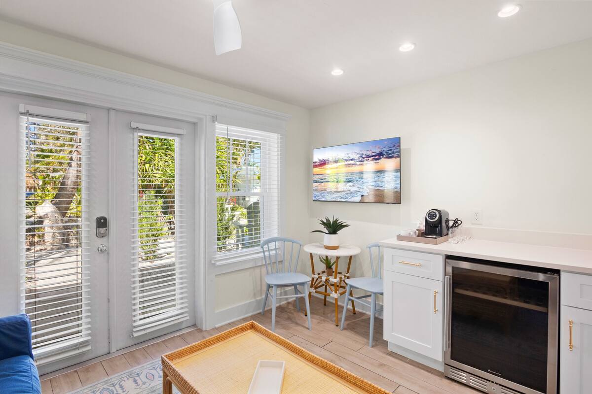 A modern kitchen with white cabinets, a built-in oven, and a dining area with blue chairs and a small round table.