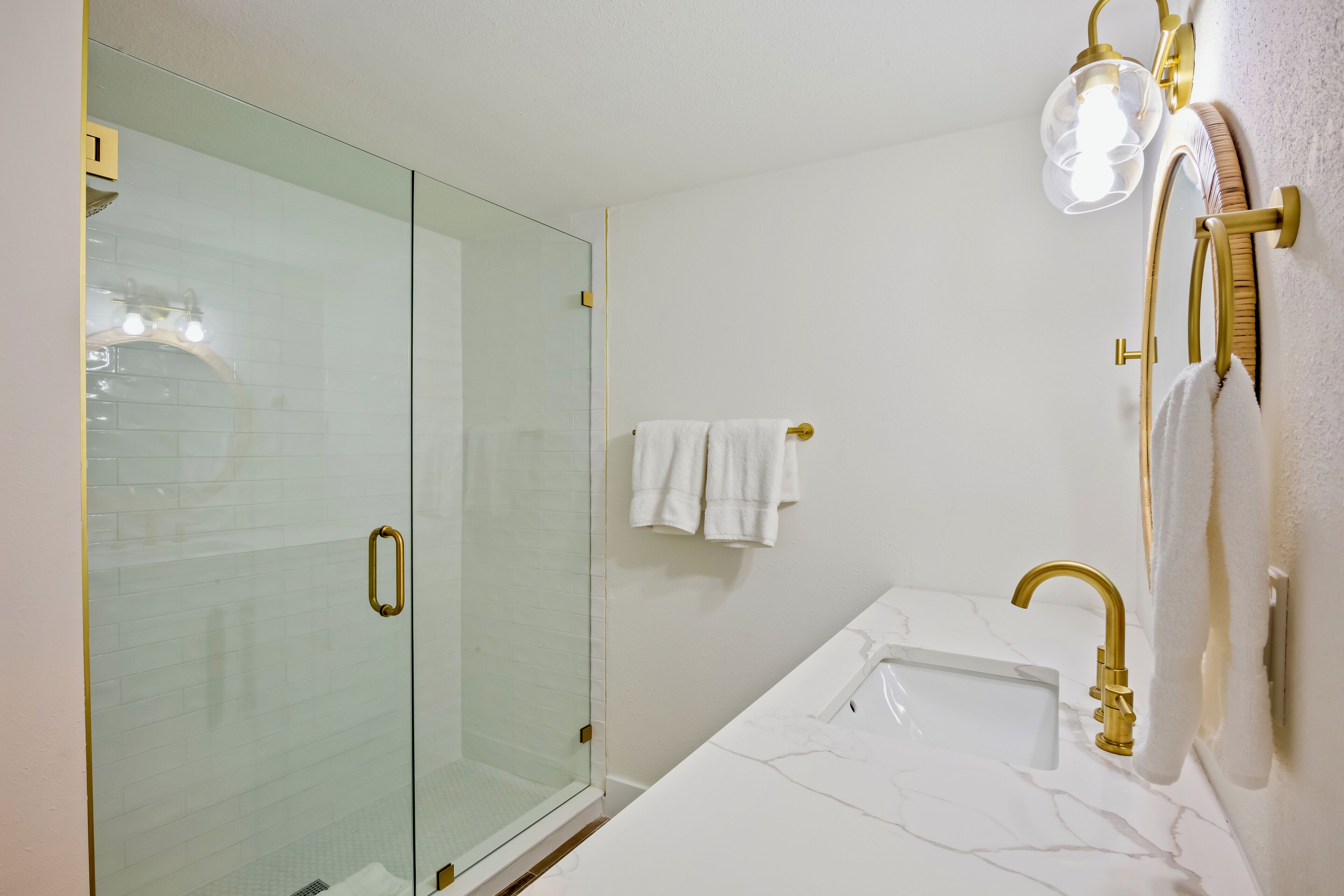 Une salle de bain avec une douche à parois de verre, un lavabo blanc avec un robinet doré et un porte-serviettes avec des serviettes blanches.