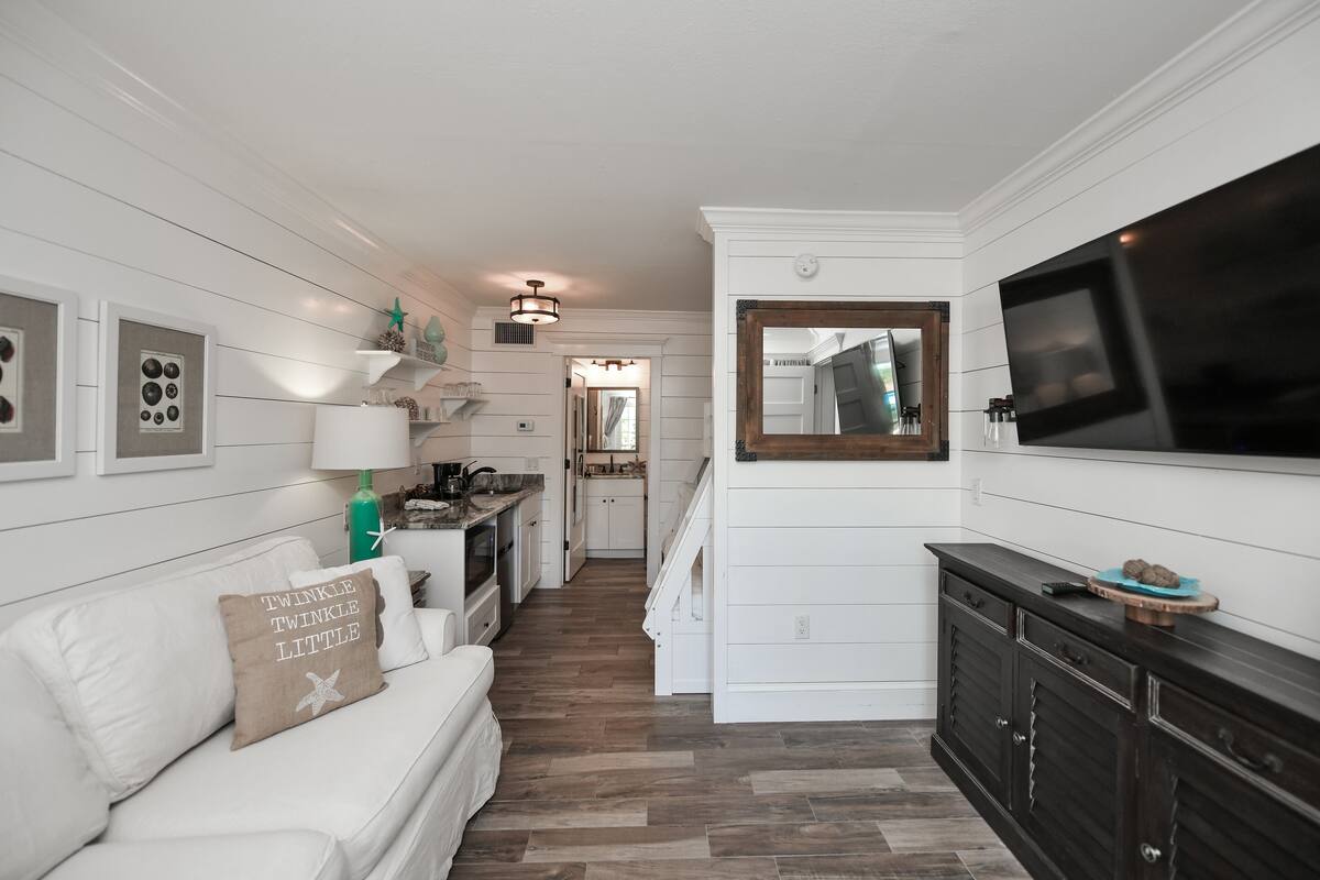 A modern kitchen with white cabinetry, a dark wooden cabinet, and a large flat-screen TV mounted above the counter.
