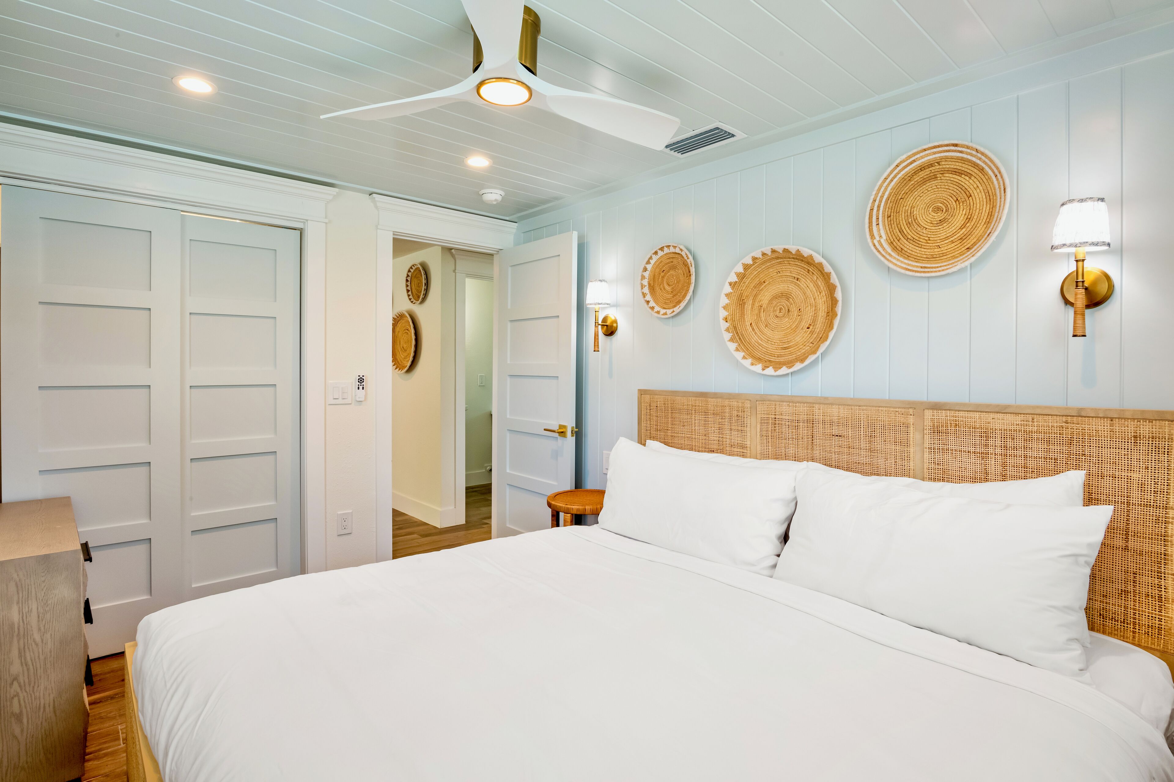Un dormitorio con una cama grande, ropa de cama blanca, un cabecero de madera y apliques de luz en la pared.