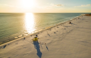 An aerial view of a beach with people, a lifeguard tower, and clear skies.