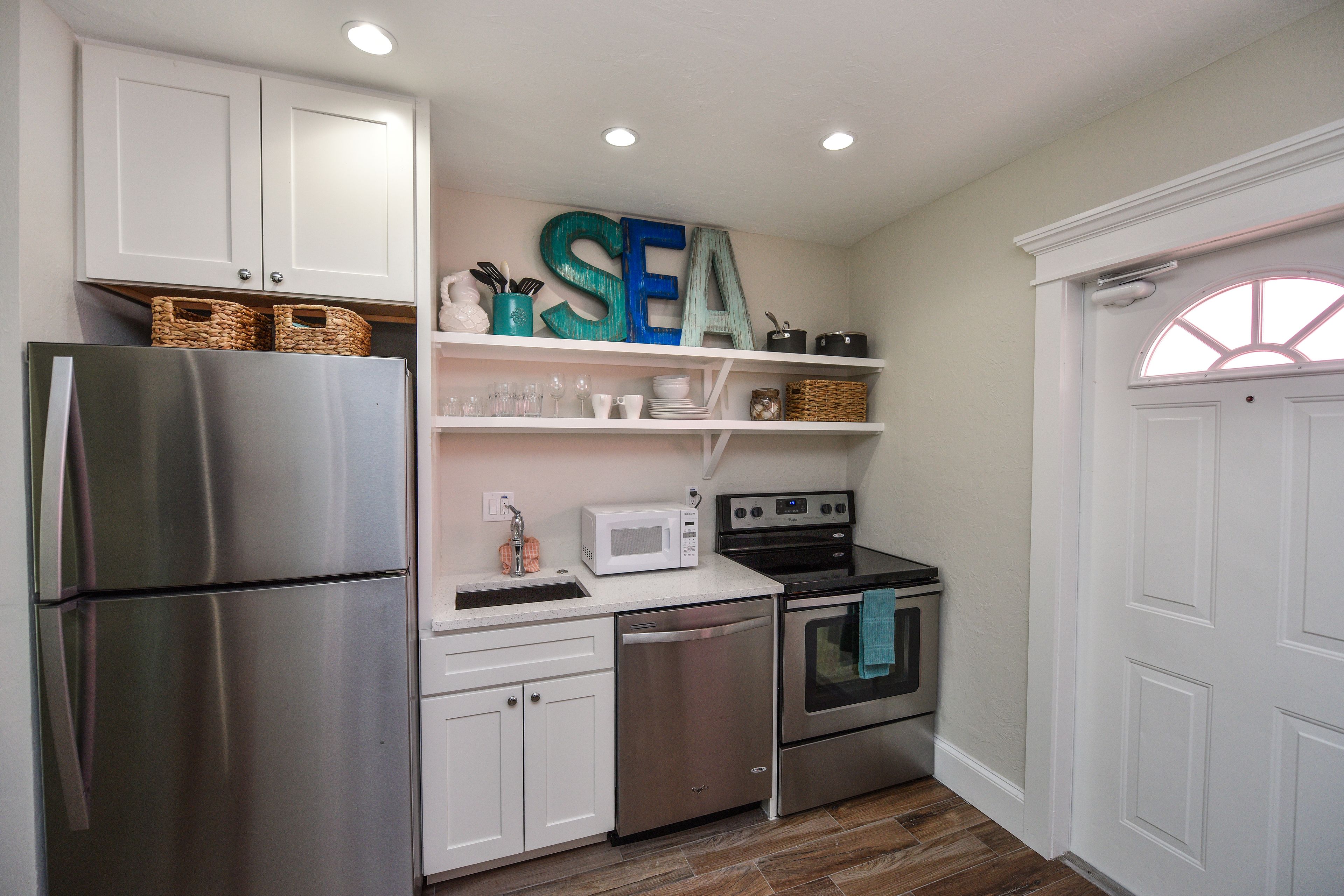A compact kitchen with white cabinetry, a stainless steel refrigerator, a microwave, an oven, and a sink.