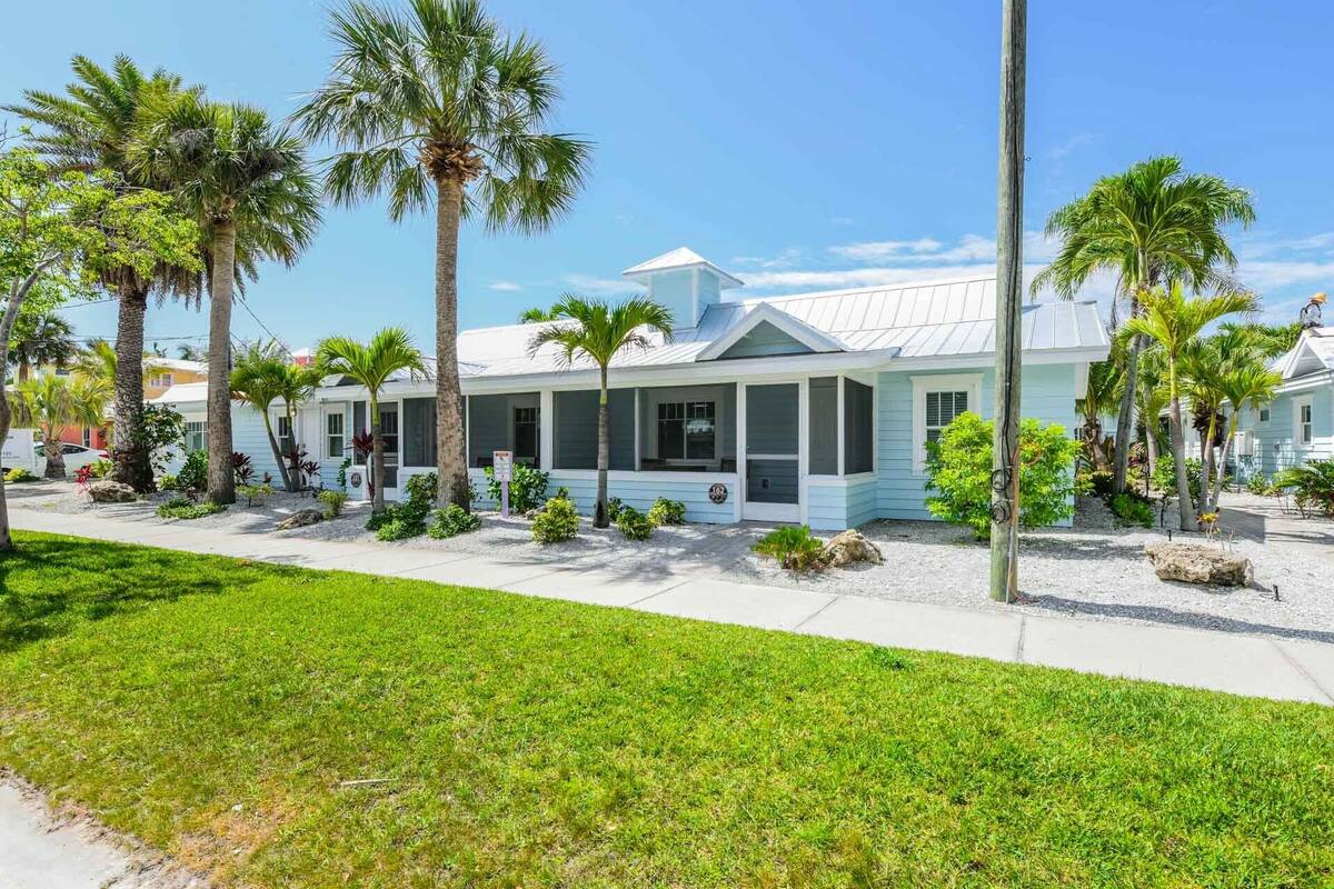 A coastal building with a covered porch, surrounded by palm trees and a grassy lawn.