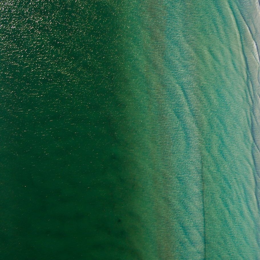 An aerial view of a beach with clear turquoise water and a sandy shore.