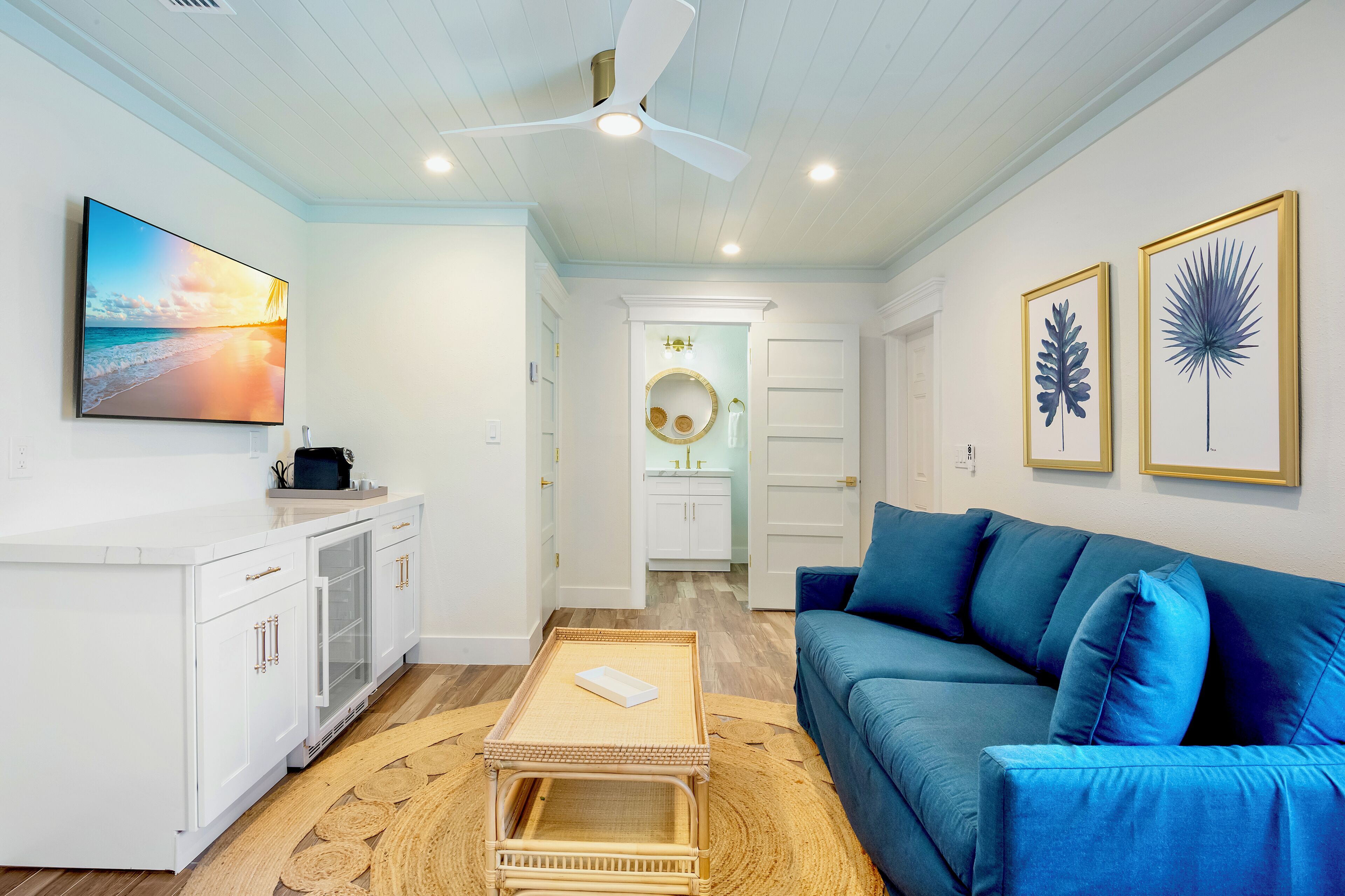 Un salon moderne avec un canapé bleu, un meuble blanc, un ventilateur de plafond et un grand tableau accroché au mur.