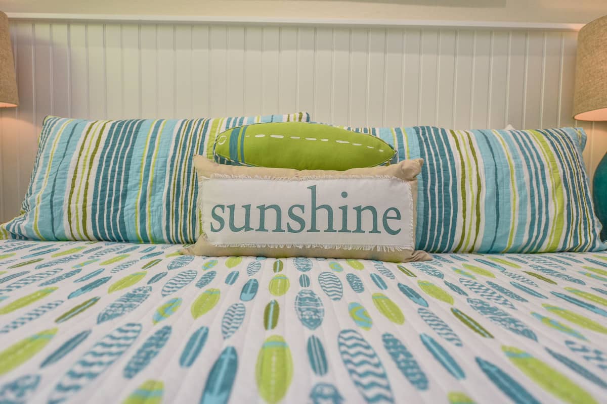 A bed with striped pillows and a pillow with the word "sunshine".