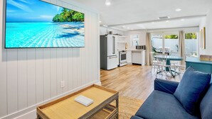 A modern living room with a large flat-screen TV, a sofa, and a dining area with a table and chairs. - Tropical Breeze Resort (Siesta Key)