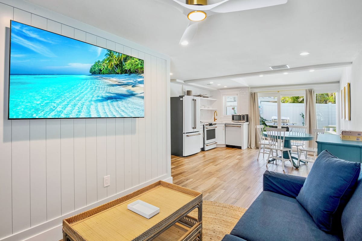 A modern living room with a large flat-screen TV, a sofa, and a dining area with a table and chairs.